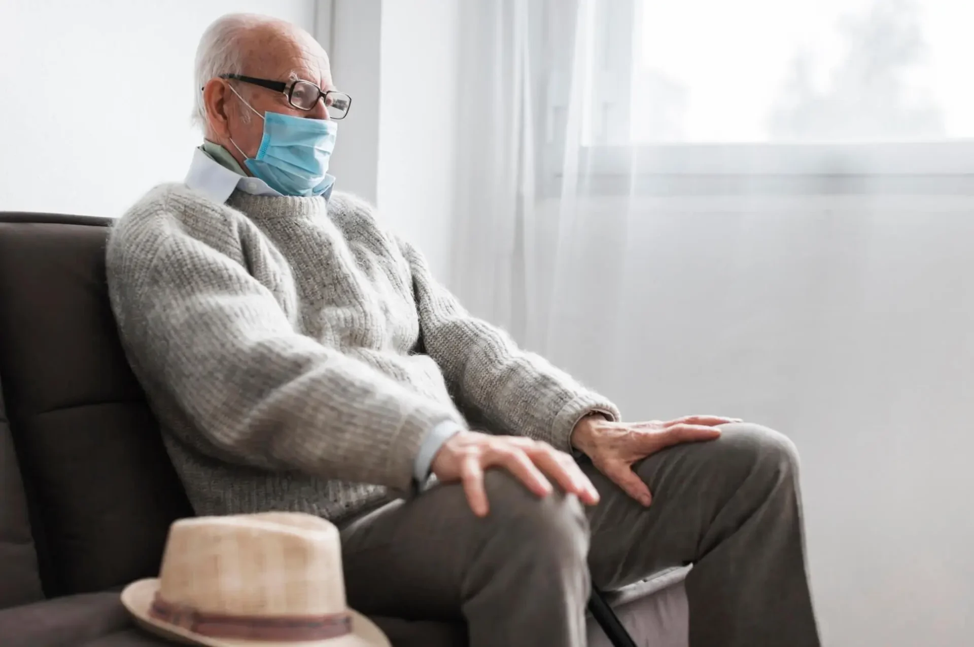 old man sitting on the couch with covid mask on his face old man sitting on the couch with covid mask on his face